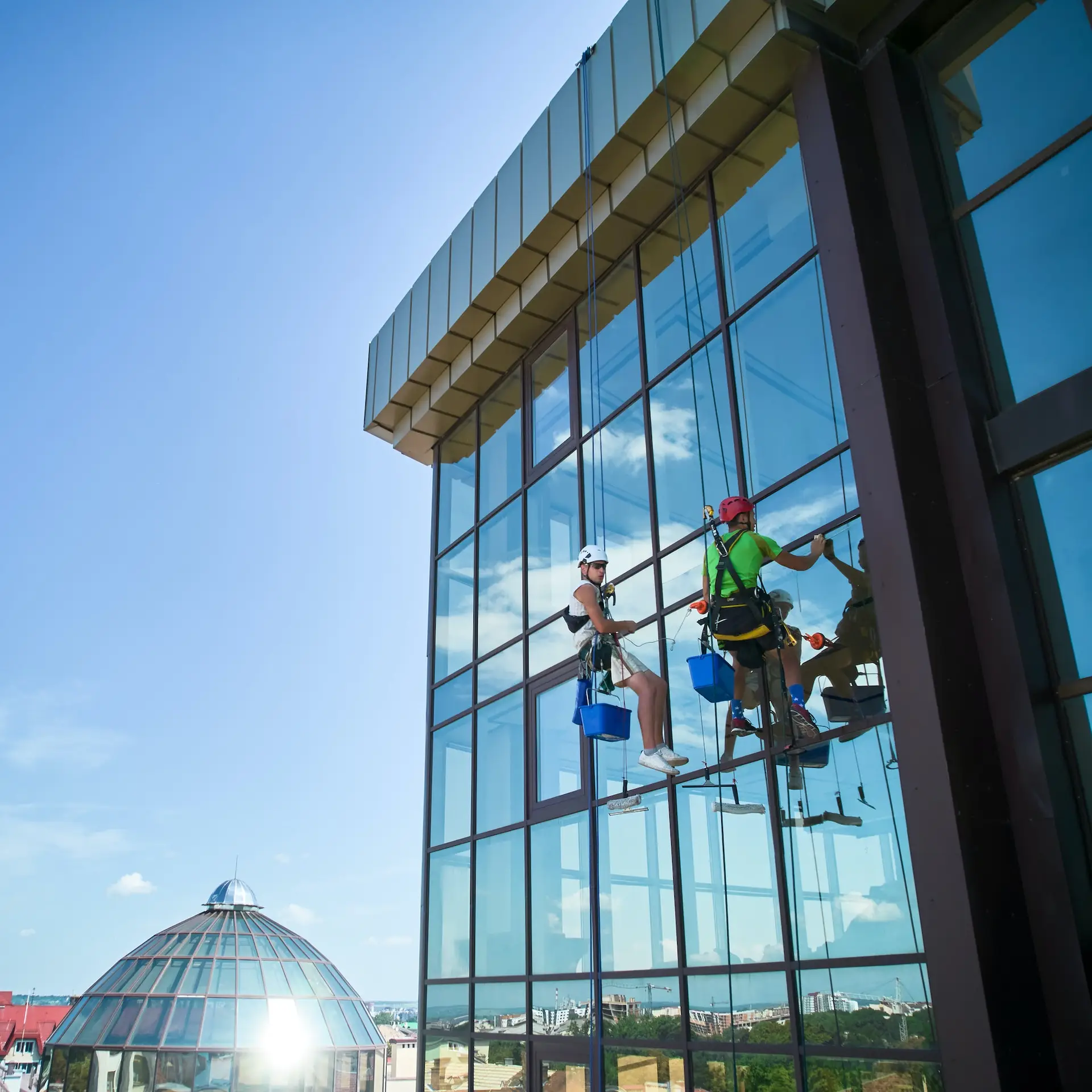 Industrial mountaineering worker cleaning window outside building.